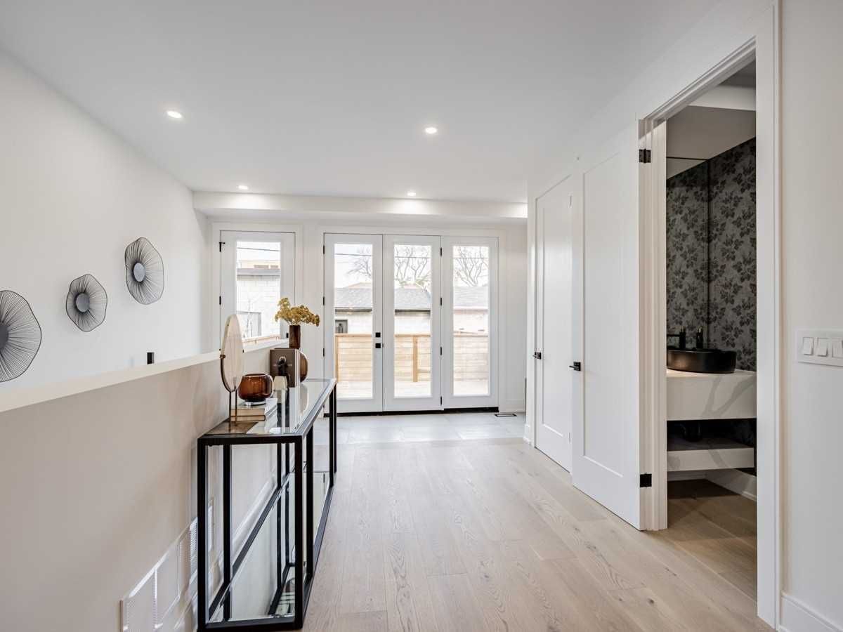 A hallway in a house with hardwood floors and white walls leading to a bathroom.