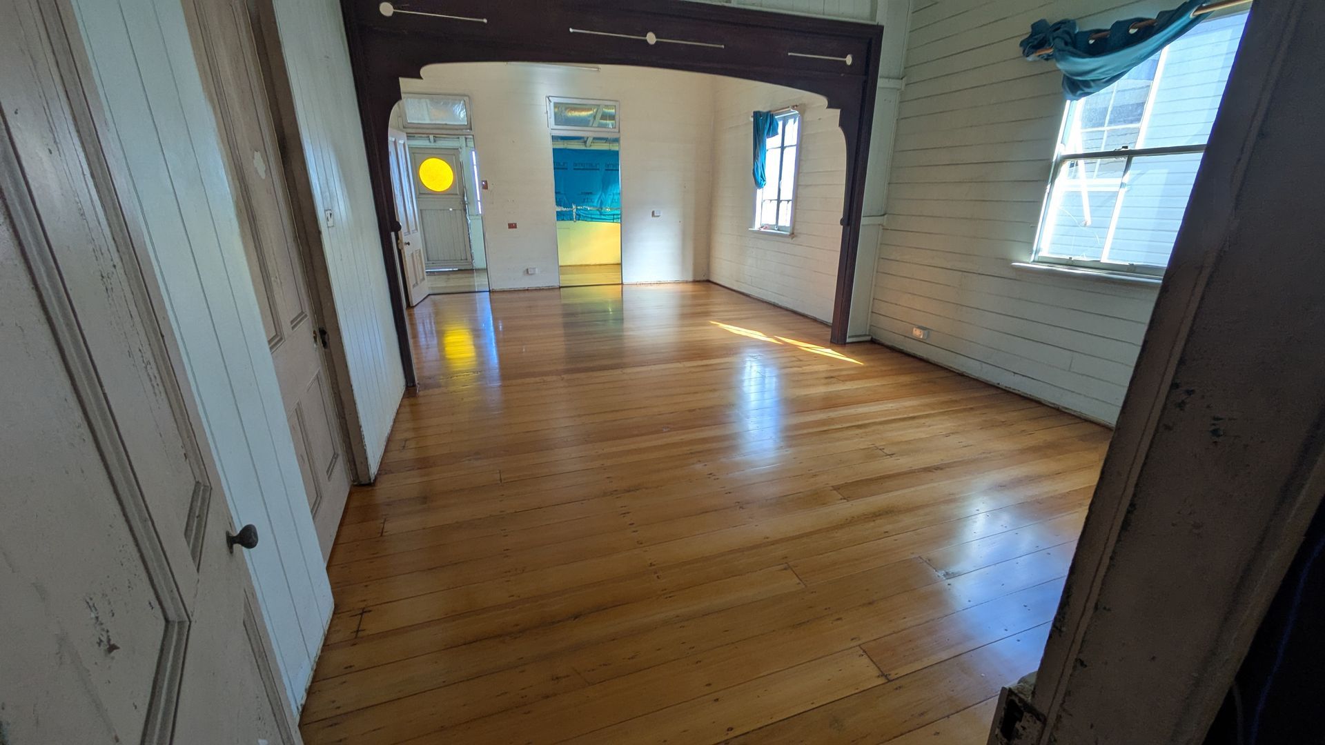 Interior of a room with polished wooden floor, doorway, and windows with natural light.