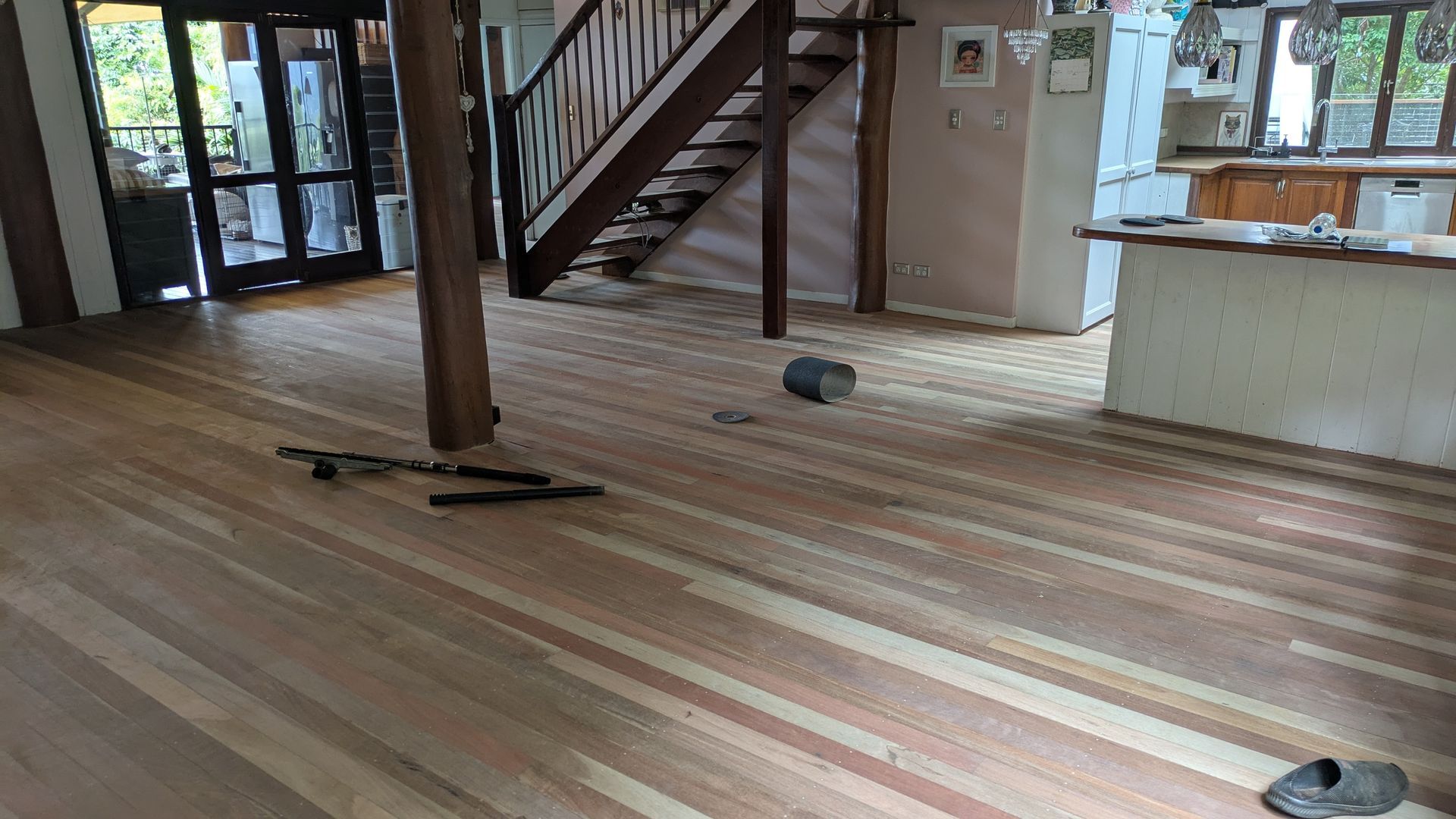 Wooden floor in home with a staircase, support beams and kitchen area in the background.