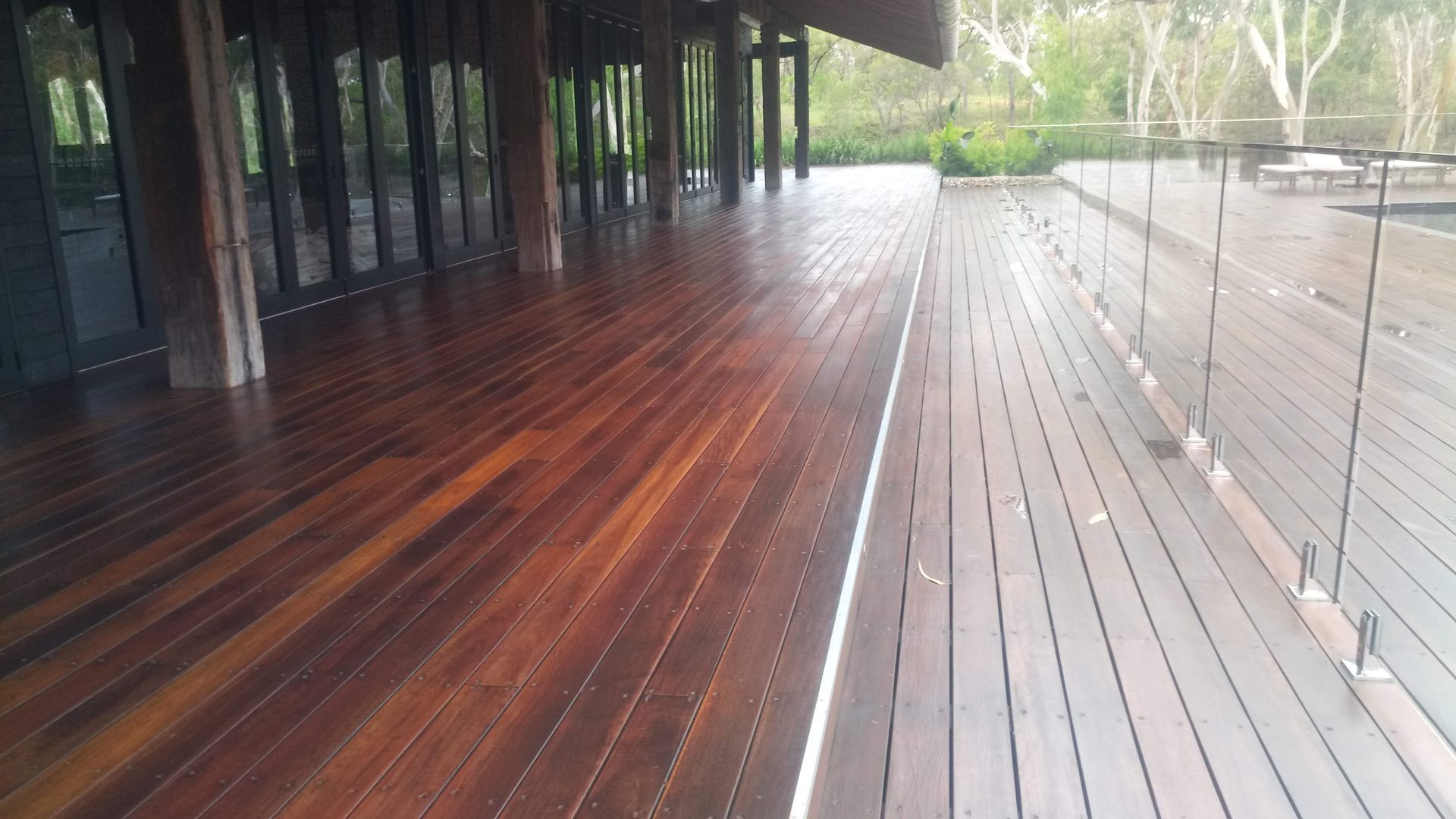 Wooden deck, glass railing, and building with dark wood doors.