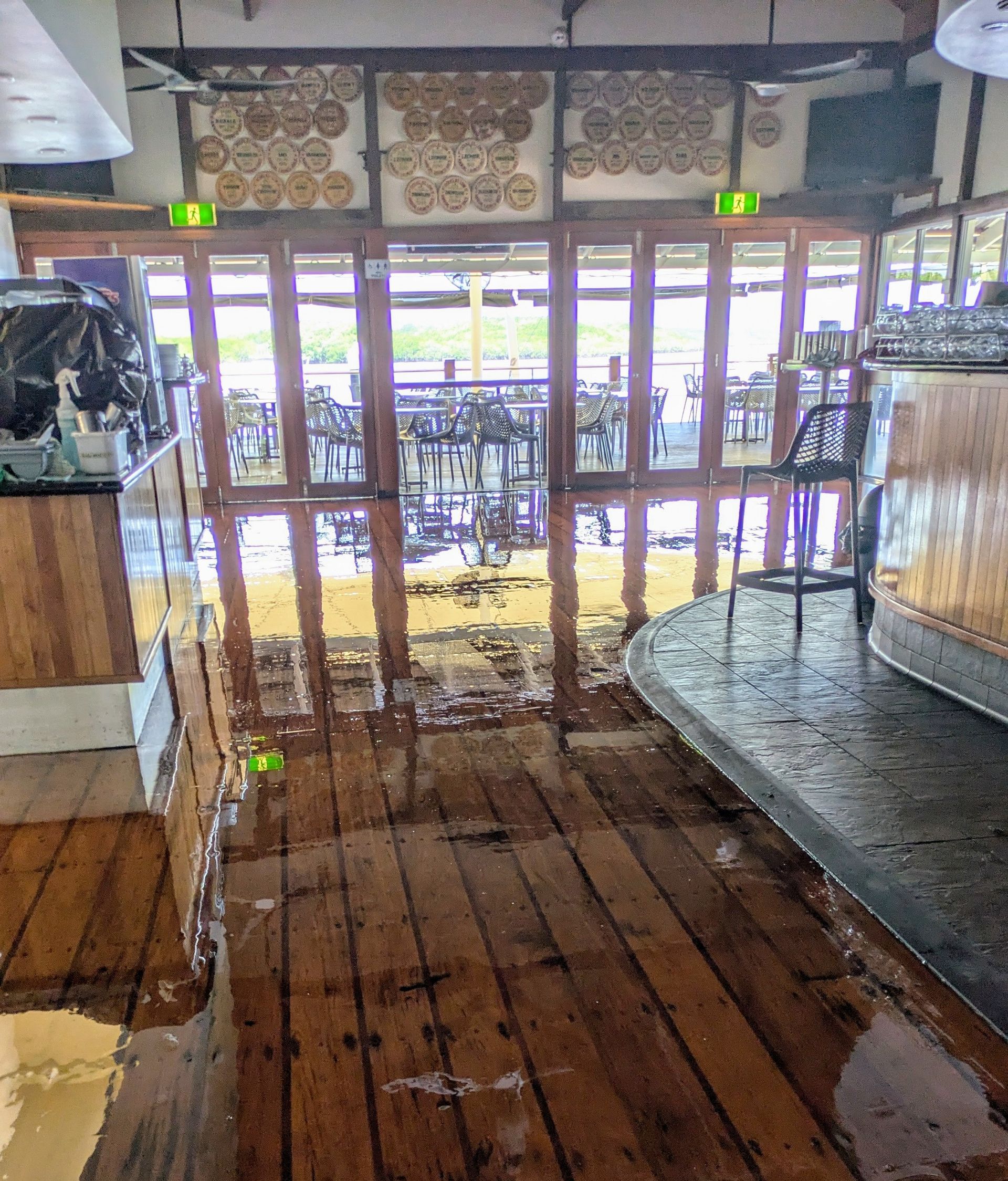 Flooded restaurant interior, wooden floors, water covering the floor, tables visible through windows.