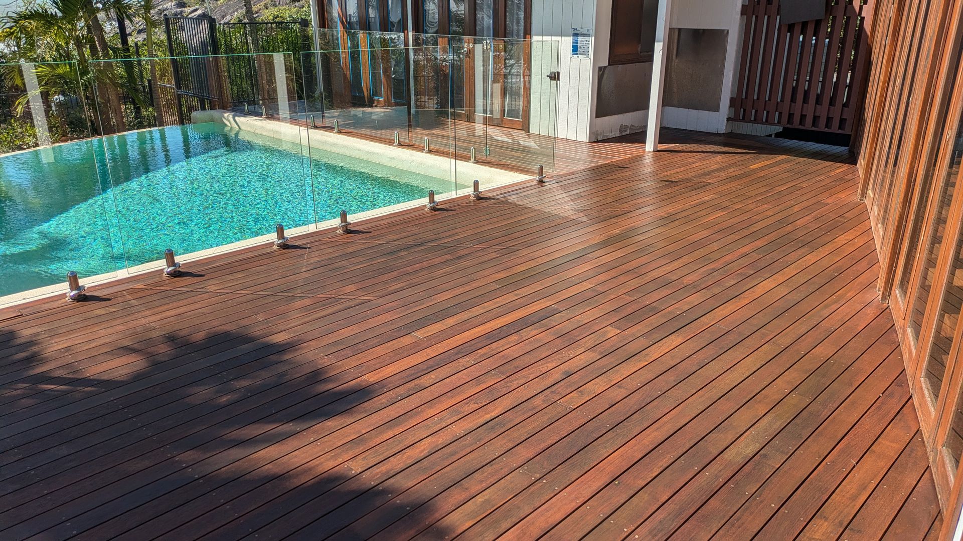 Wooden deck next to a pool with clear glass fencing.
