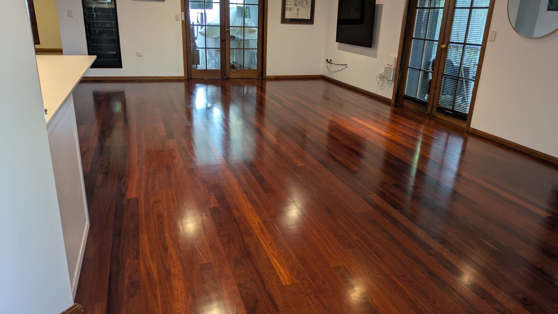 Polished, reddish-brown hardwood floor reflecting light; a room with double doors and a window.