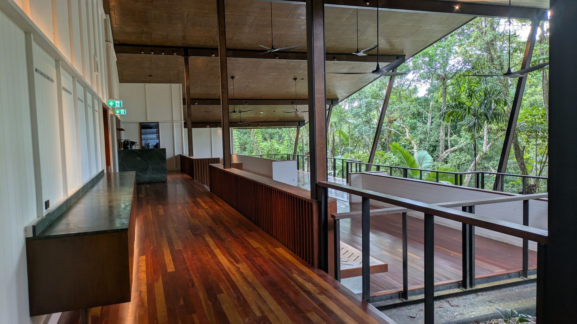 Wooden deck with a view of lush green trees, overlooking a forest. Interior of a building.
