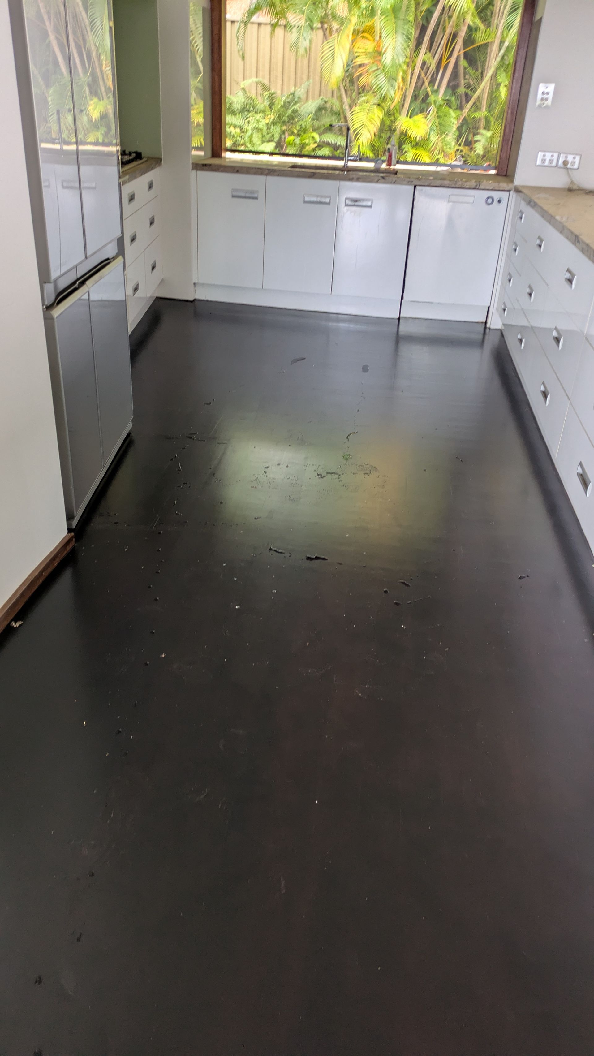 Kitchen with dark gray floor, white cabinets, and a window overlooking greenery.