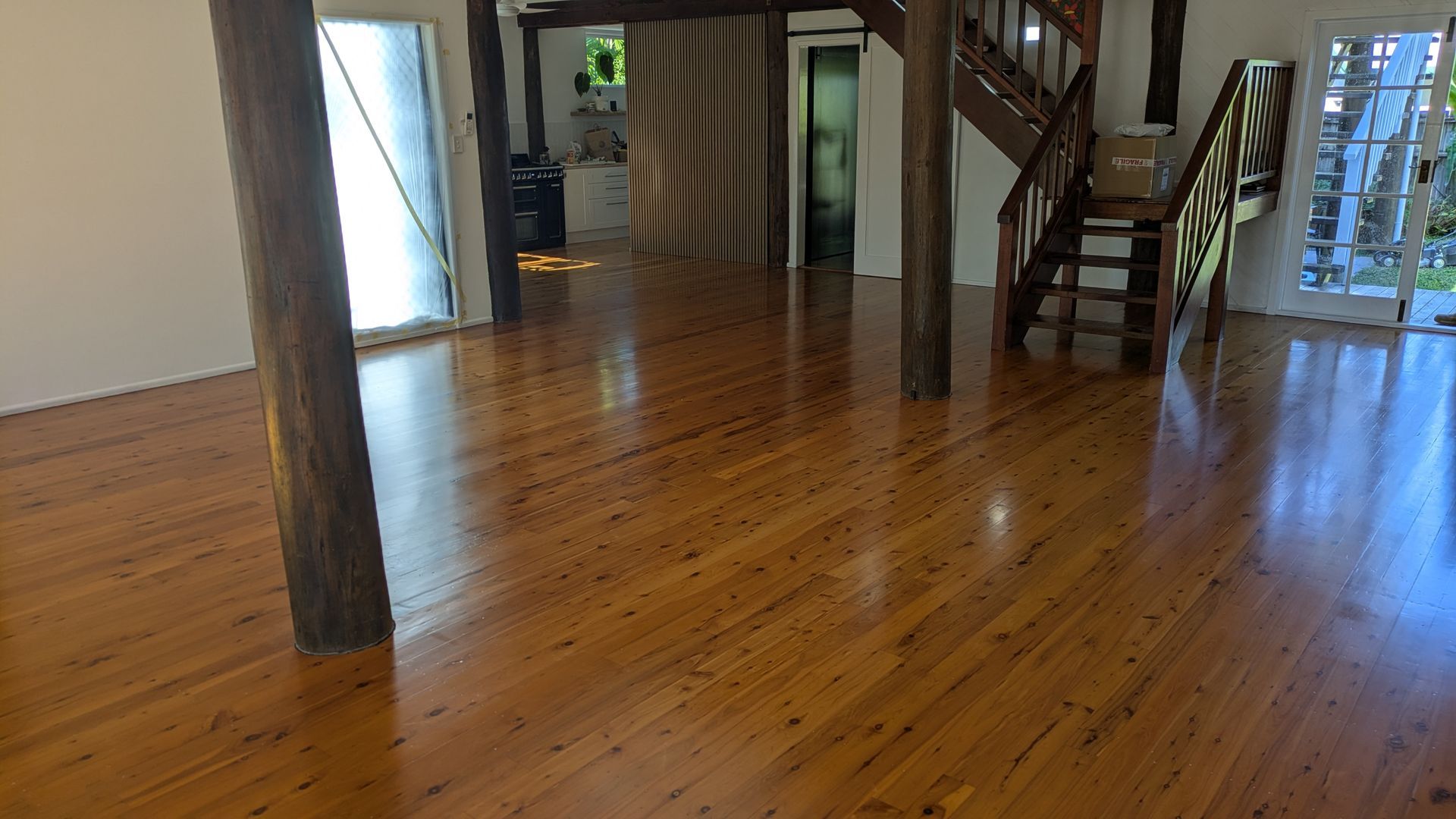 Wooden floor in a bright room with exposed support beams and stairs leading upward.