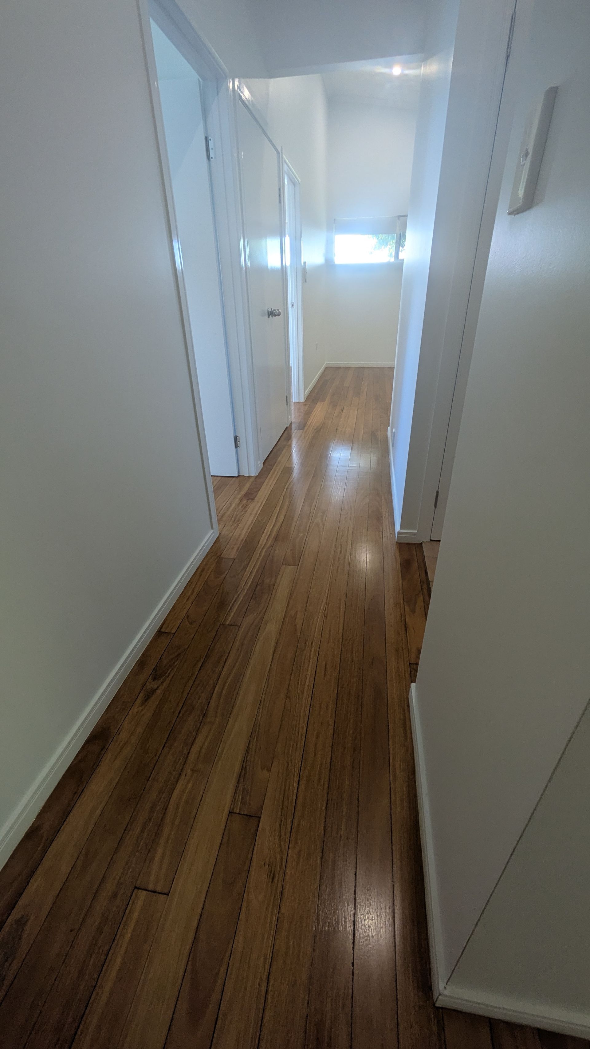 Narrow hallway with wood floor, white walls and doors.