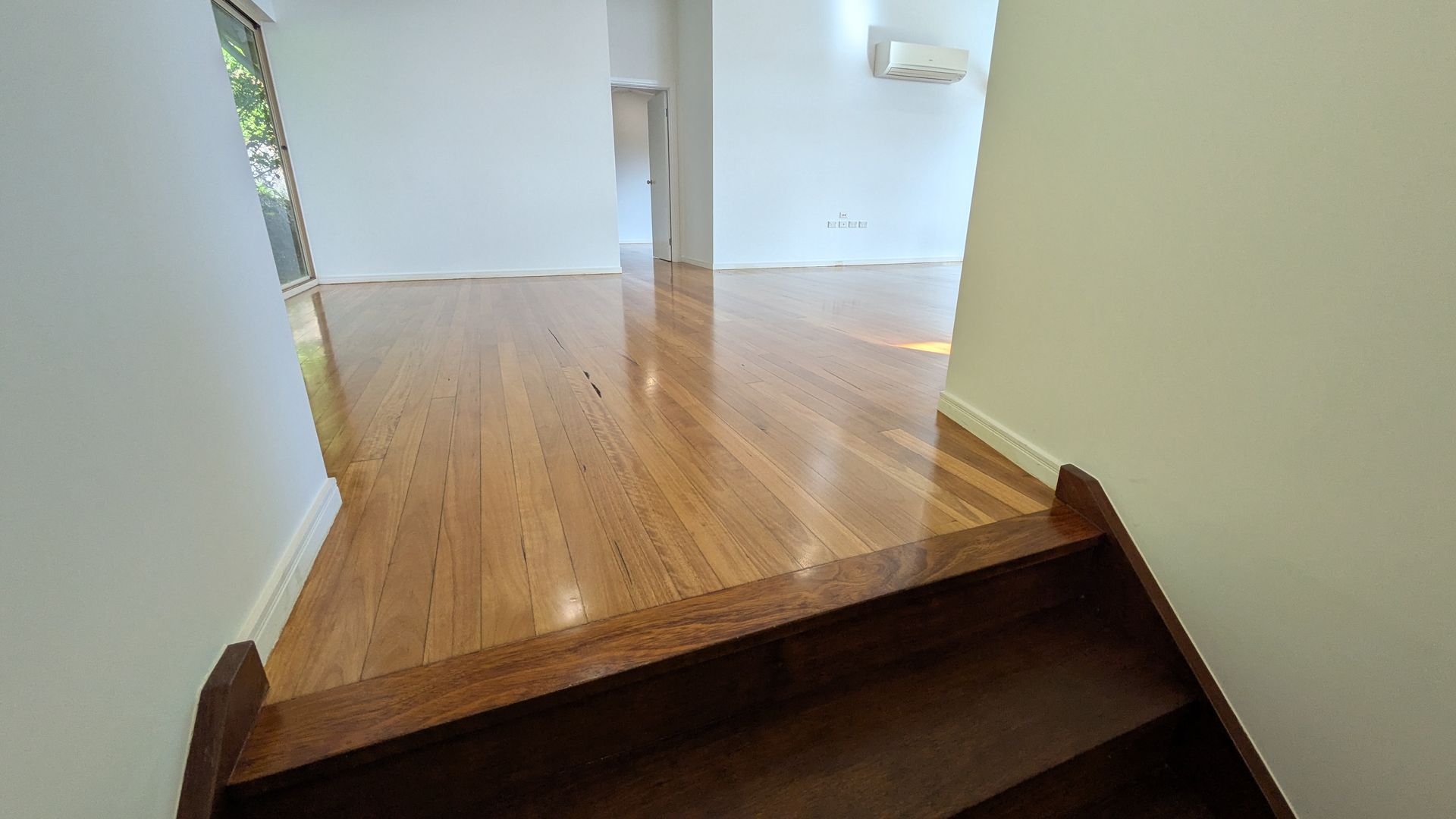 Wooden stairs lead up to a hallway with polished hardwood floors and white walls.