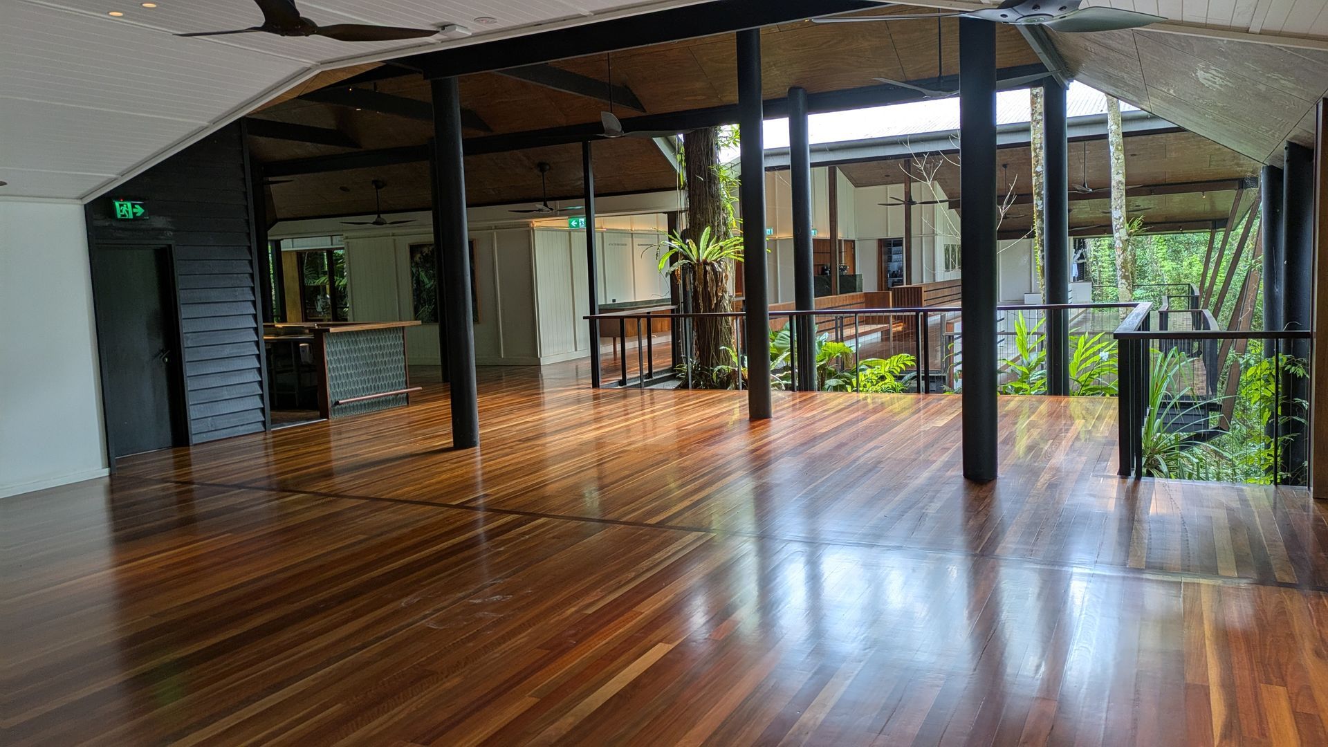Wooden floored interior with black pillars and open-air view of foliage and structures.