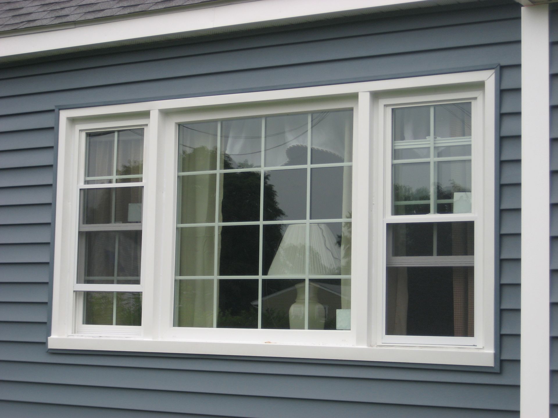 White-framed window on a blue-sided house with a grid pattern, three panes.