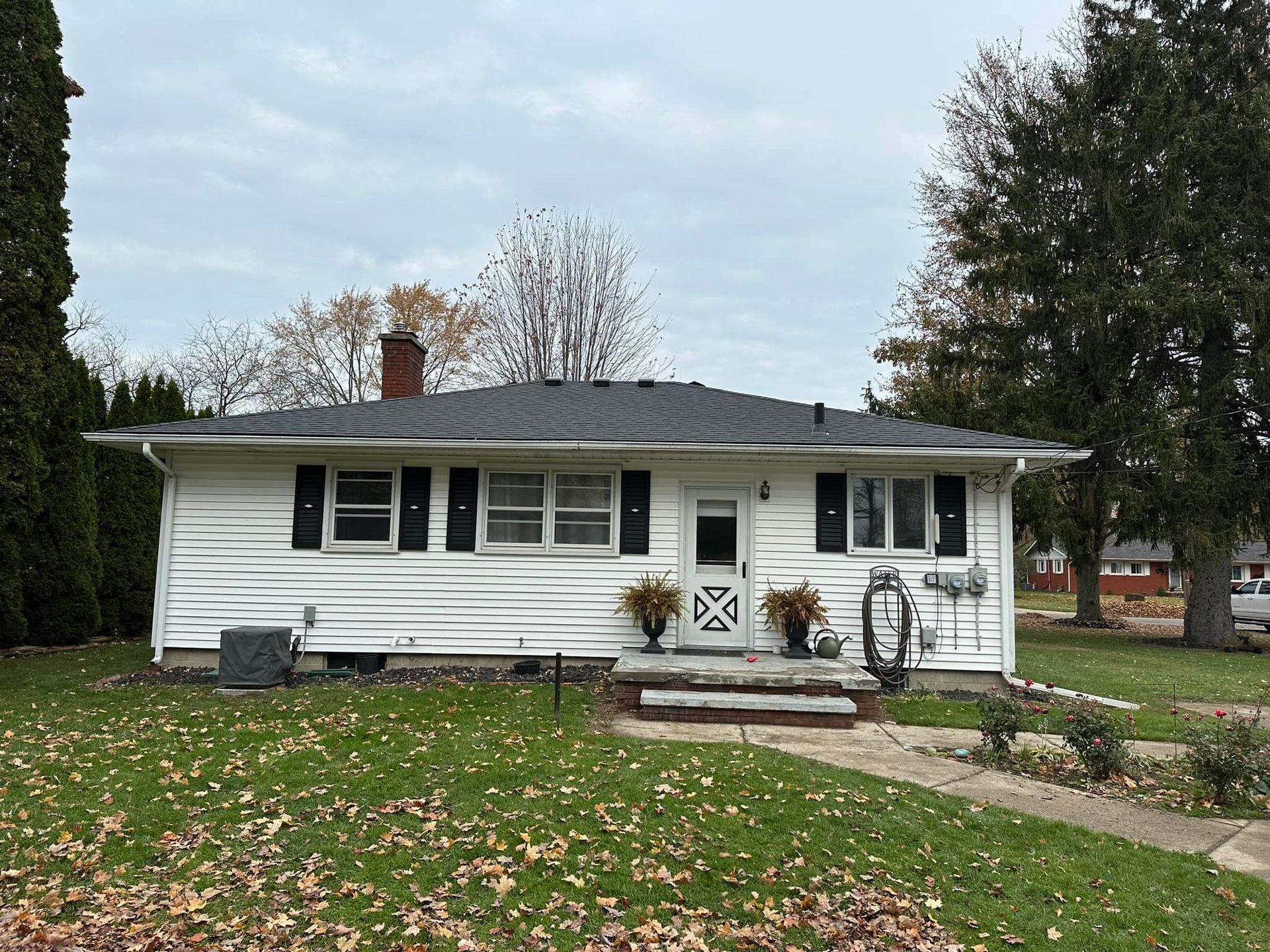 A white house with a black roof is sitting on top of a lush green lawn.