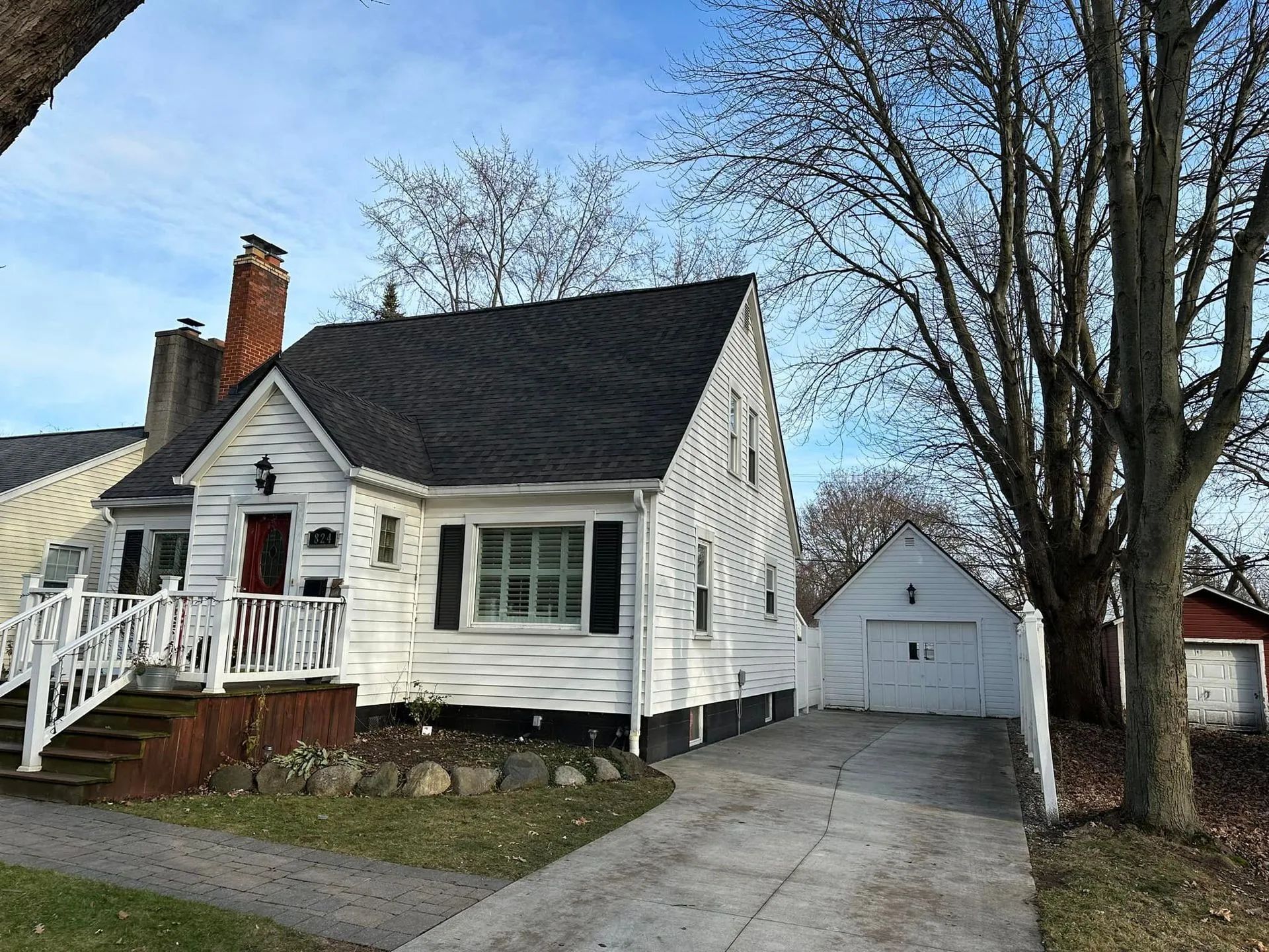 White house with a porch and chimney, next to a driveway and garage.