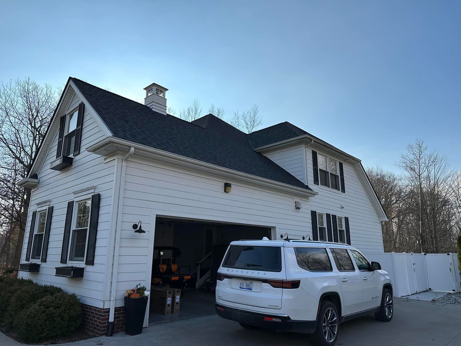 A white suv is parked in front of a white house with a black roof.