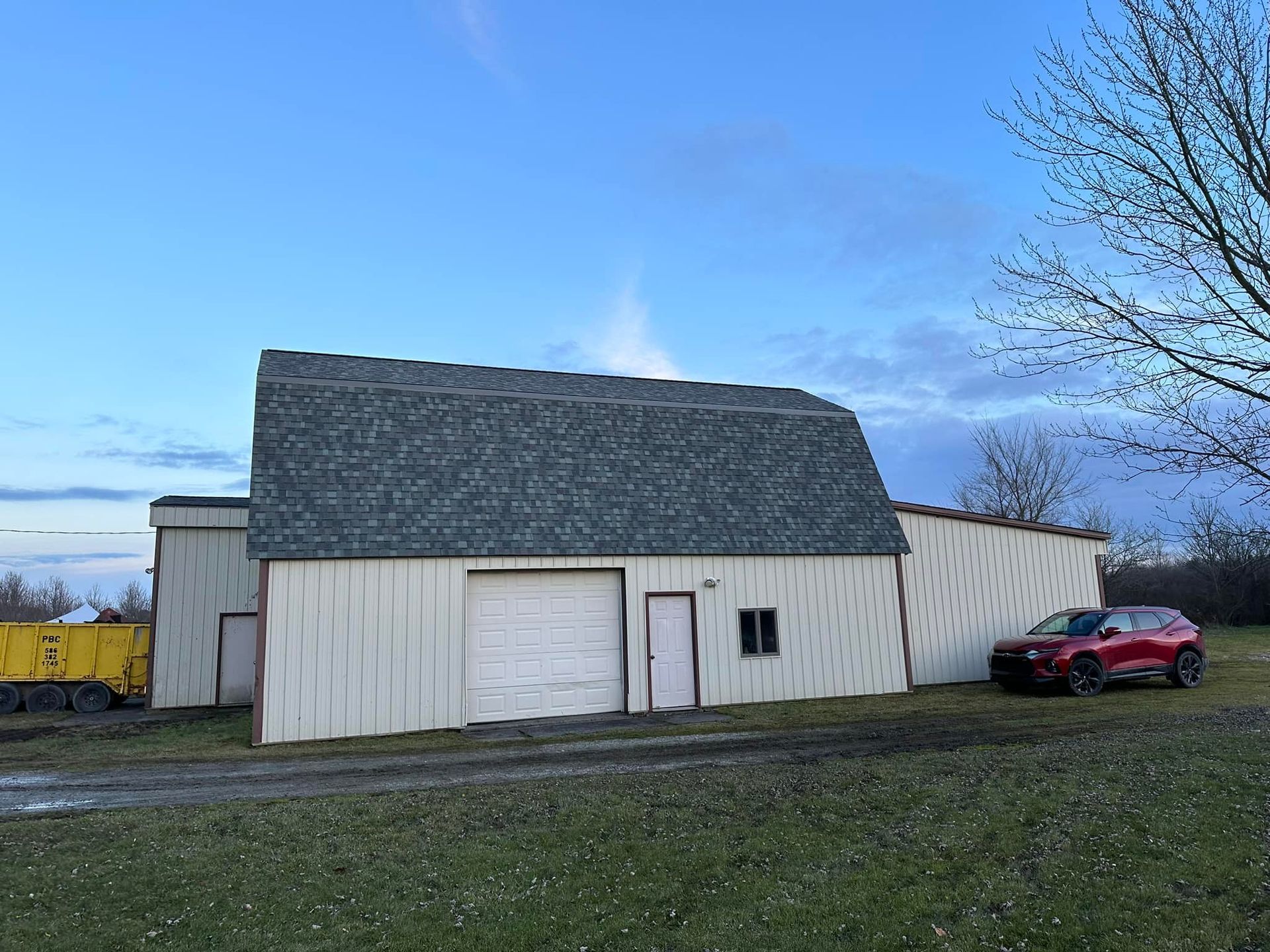 A red truck is parked in front of a white barn.