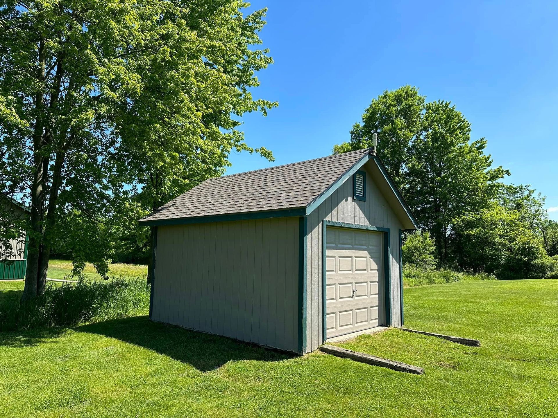 A small garage is sitting in the middle of a grassy field.