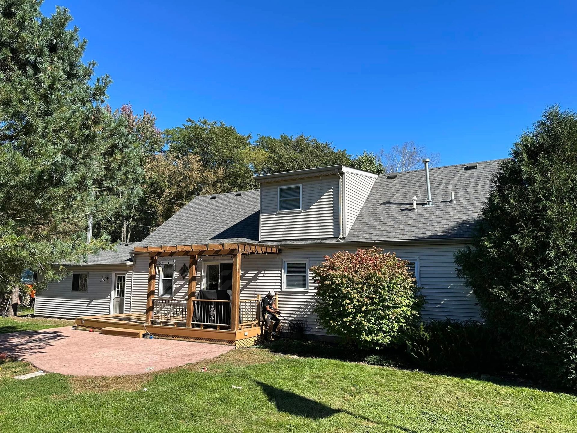 A white house with a gray roof and a deck in the backyard.