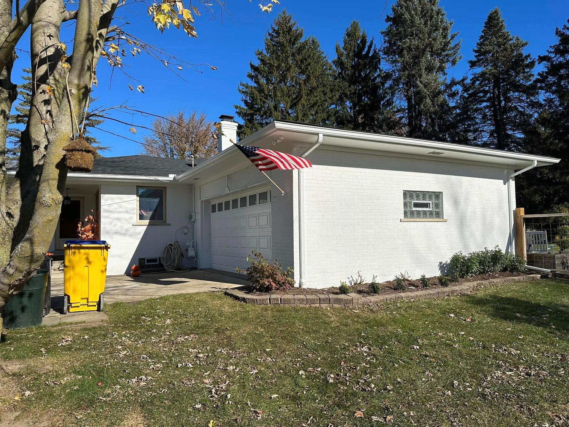 A white house with a yellow trash can in front of it.