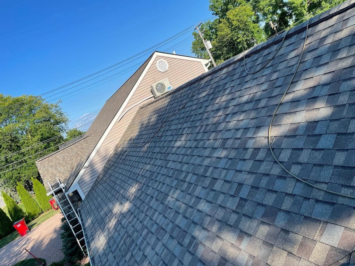 Shingled house roof under blue sky, with a ladder leaning against the side wall.