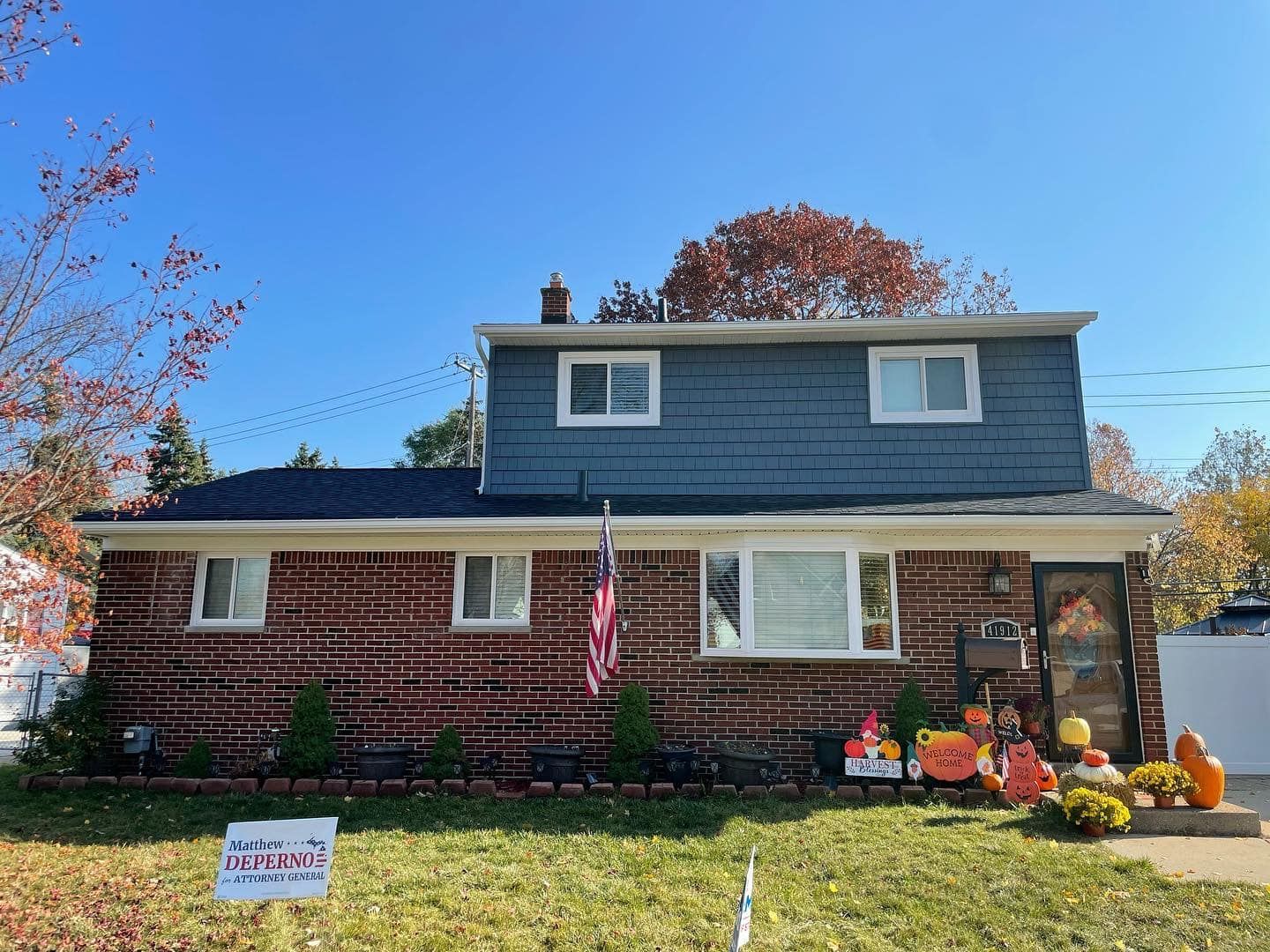 A brick house with a blue siding and a sign in front of it.