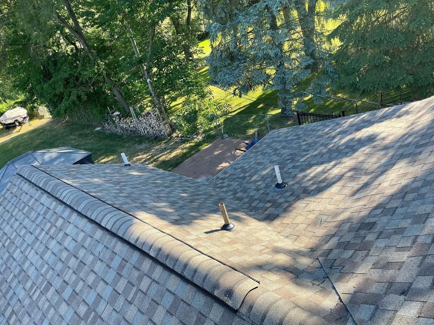 View of a house roof with shingles, vents, and a tree-filled backyard.