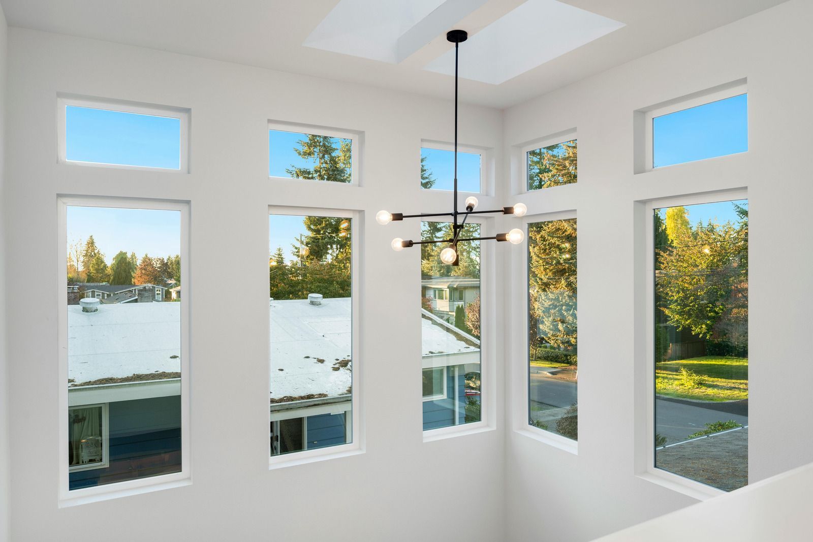 Bright, airy room with large windows overlooking a neighborhood and a modern chandelier.