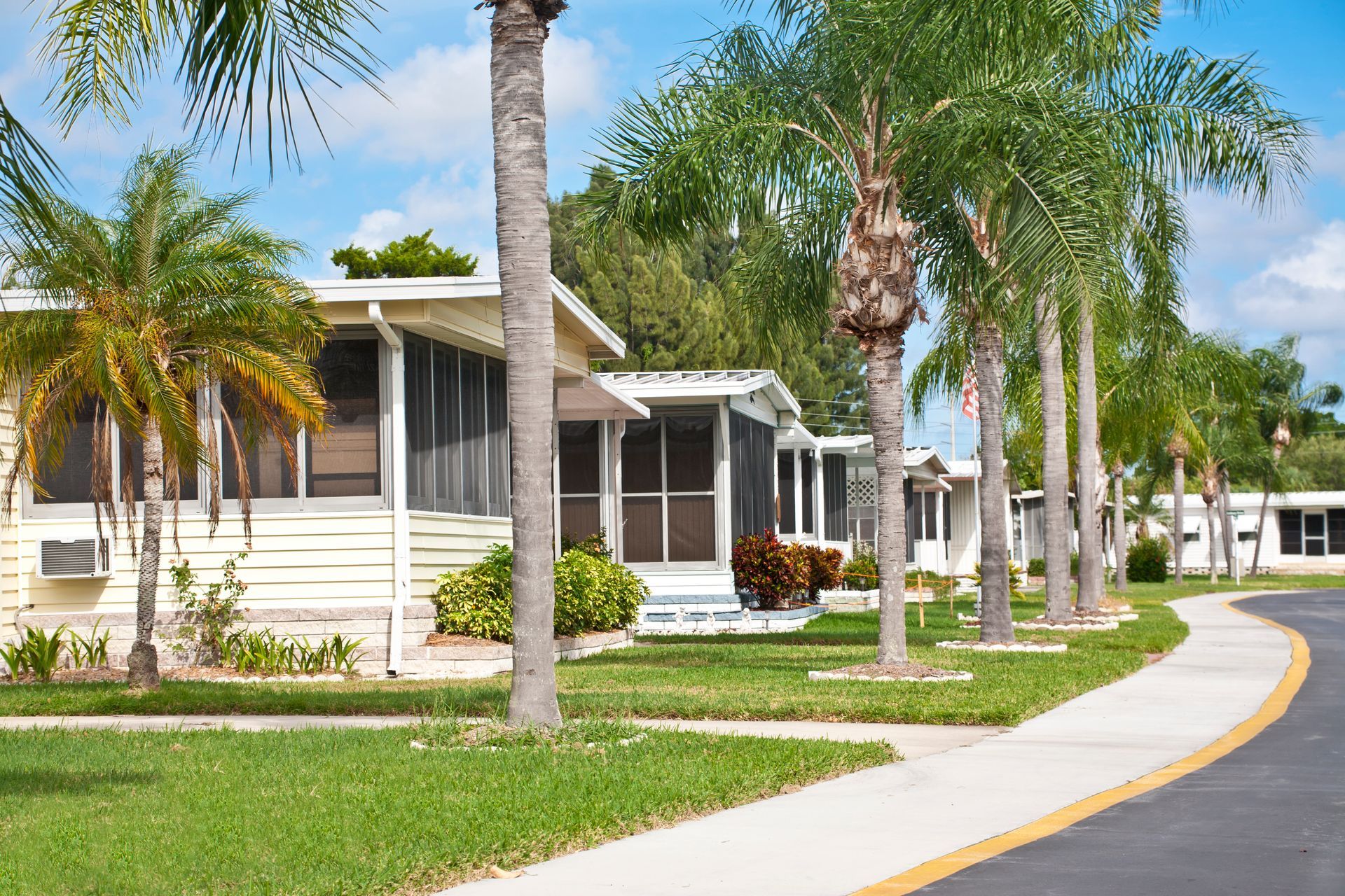 A row of mobile homes in a residential area with palm trees and a sidewalk.