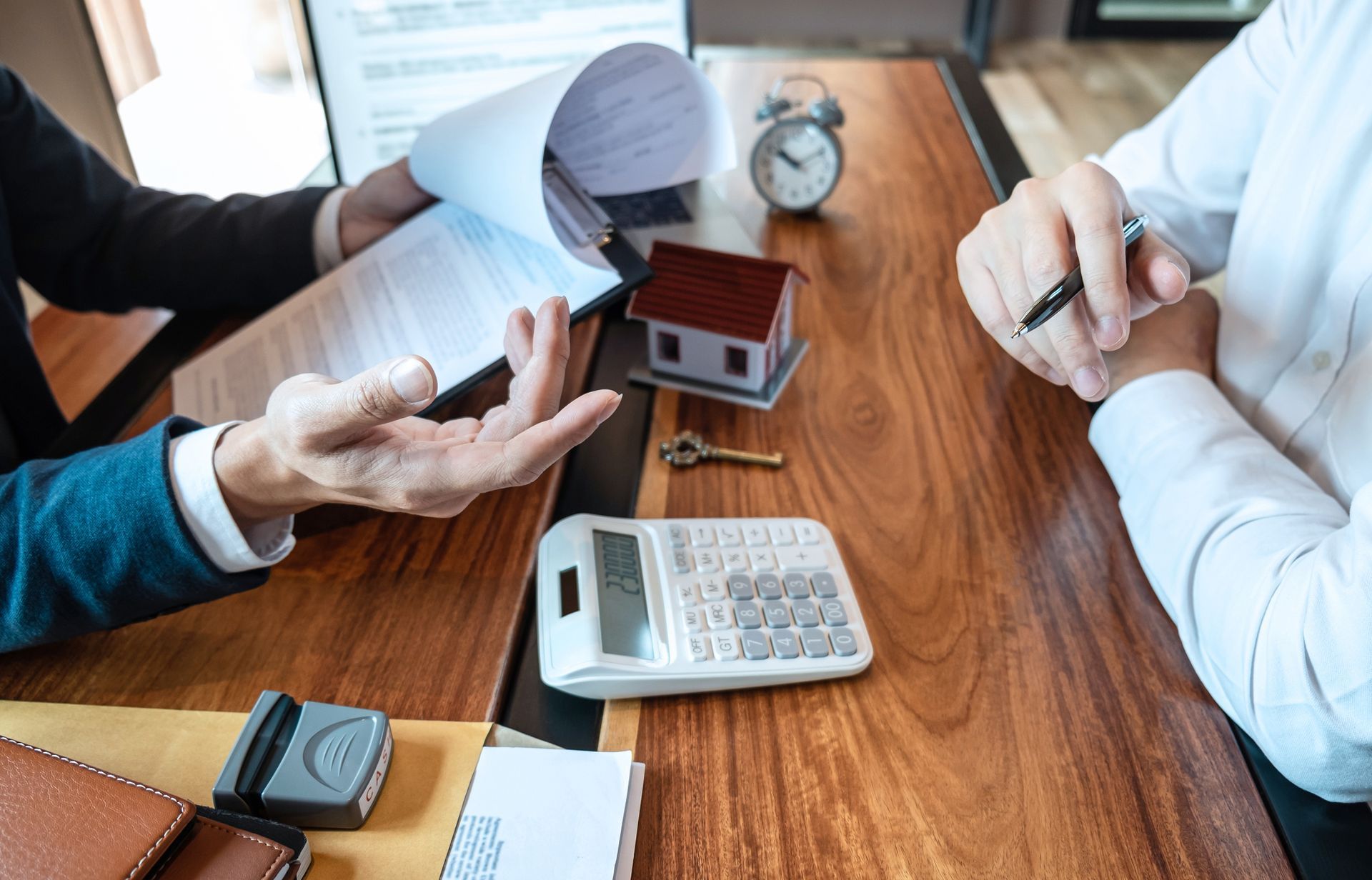Two people are sitting at a table with a calculator and a model house.