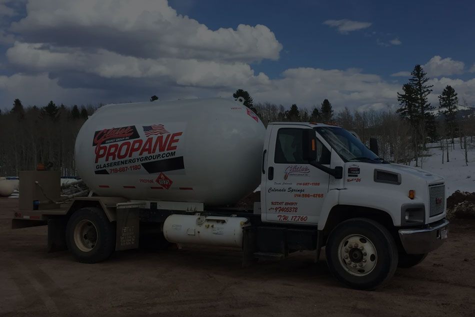 A white propane truck is parked in a dirt field.
