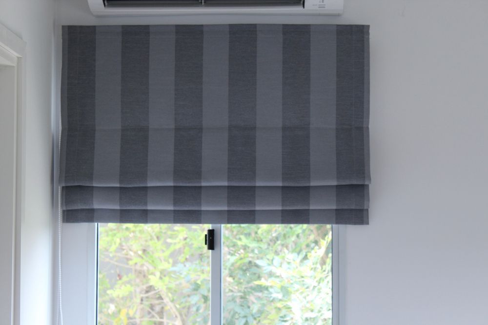 Gray striped Roman shade over a window with a view of greenery — GV Blinds in Shepparton, VIC