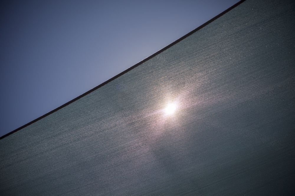 Sun Shining Through a Dark, Textured Shade Sail Against a Blue Sky — GV Blinds in Shepparton, VIC