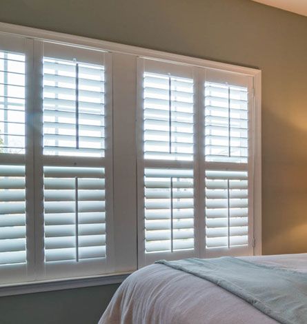 White Shuttered Windows in a Bedroom With a Blue Bedspread Against a Grey Wall — GV Blinds in Shepparton, VIC
