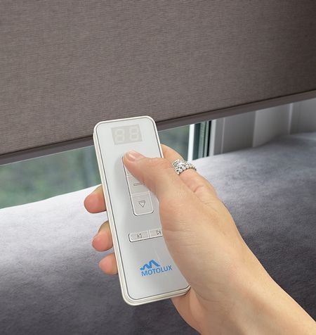 Hand Holding Remote, Controlling Grey Motorised Window Shade Near a Window — GV Blinds in Shepparton, VIC