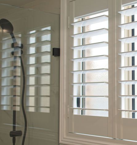 White Shutters Beside a Shower With Black Showerhead, in a Bathroom Setting — GV Blinds in Shepparton, VIC