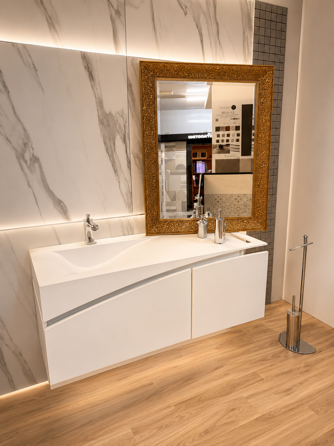 Bagno moderno con pareti in marmo, pavimento in legno, mobile lavabo bianco e specchio con cornice dorata.