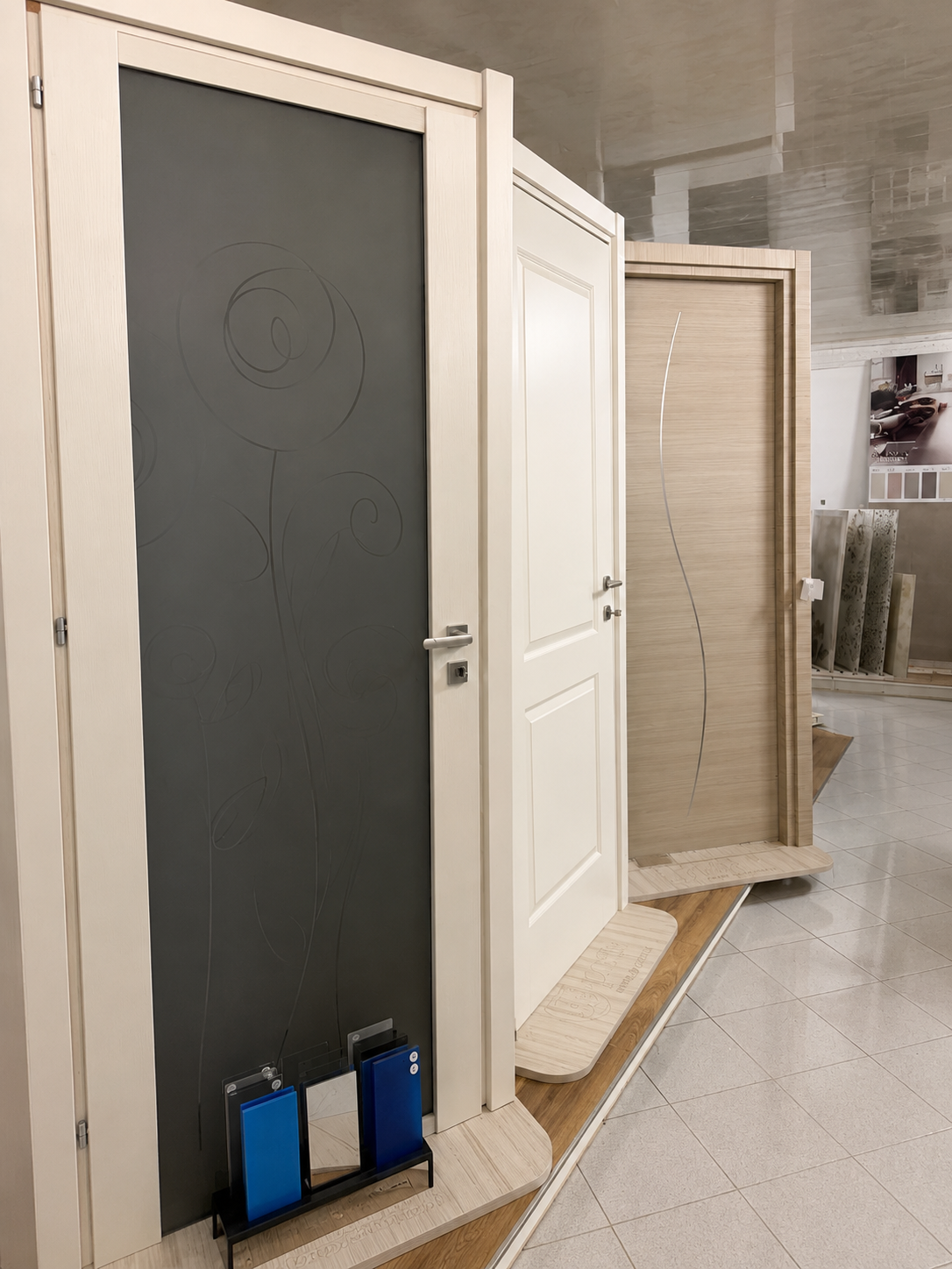Esposizione interna di tre porte, tra cui una porta grigio scuro con inserti blu alla base.