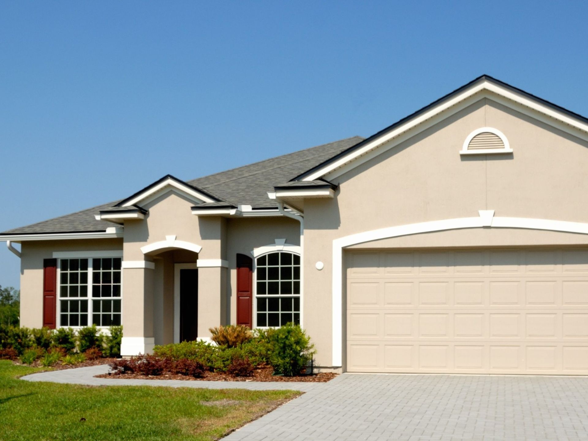 A beige house with a white garage door and red shutters
