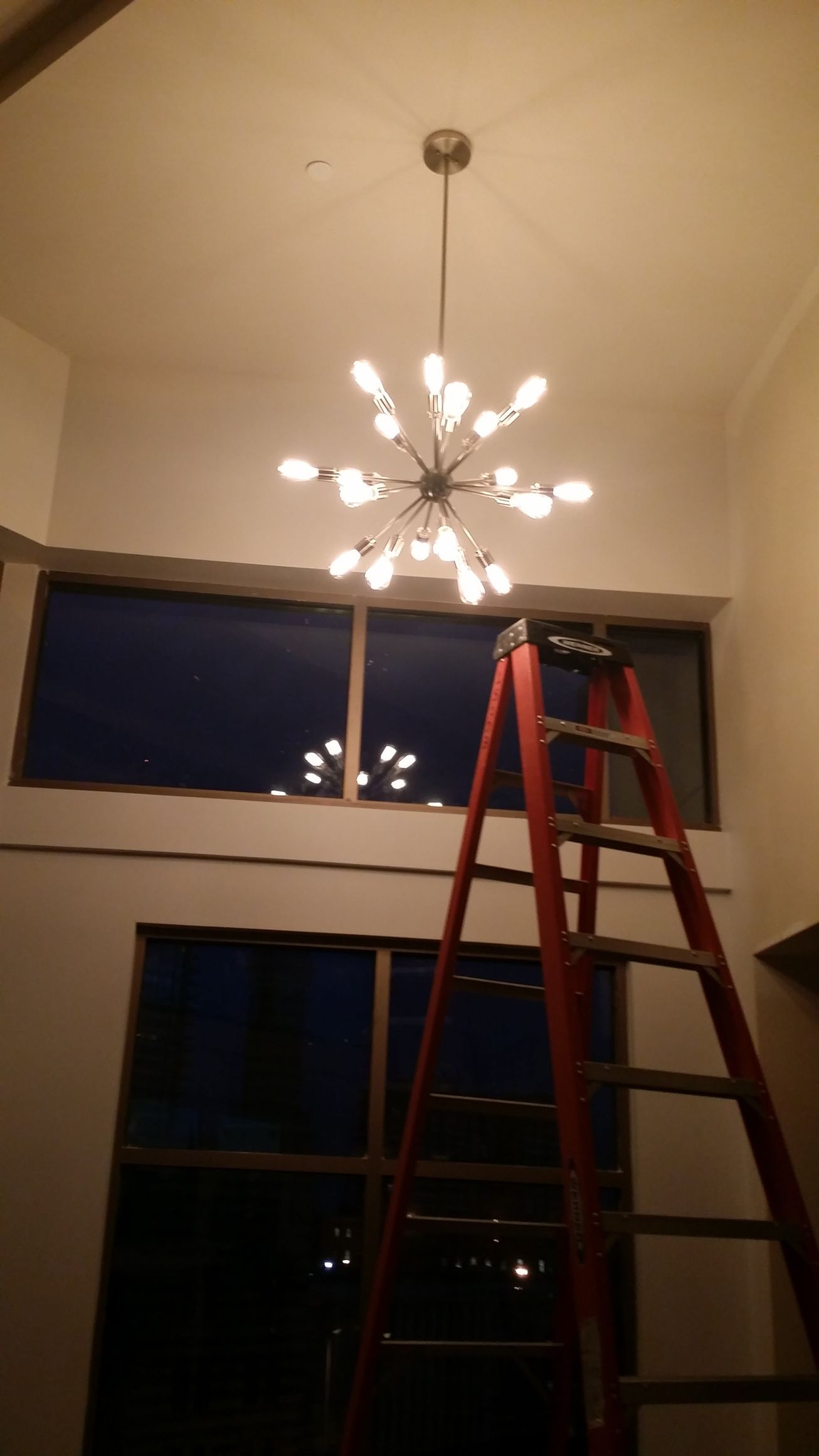 A red ladder is sitting under a chandelier in a room.