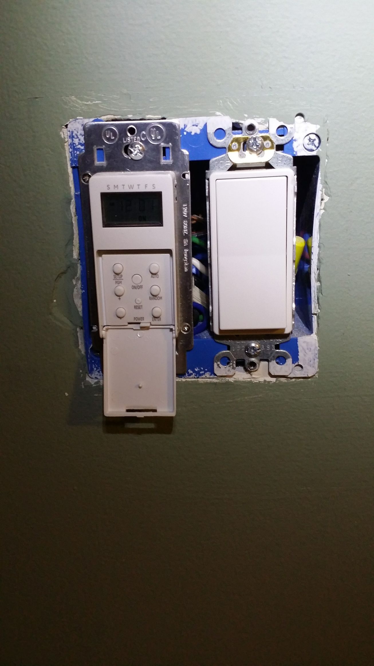 A remote control is hanging on a wall next to a light switch.