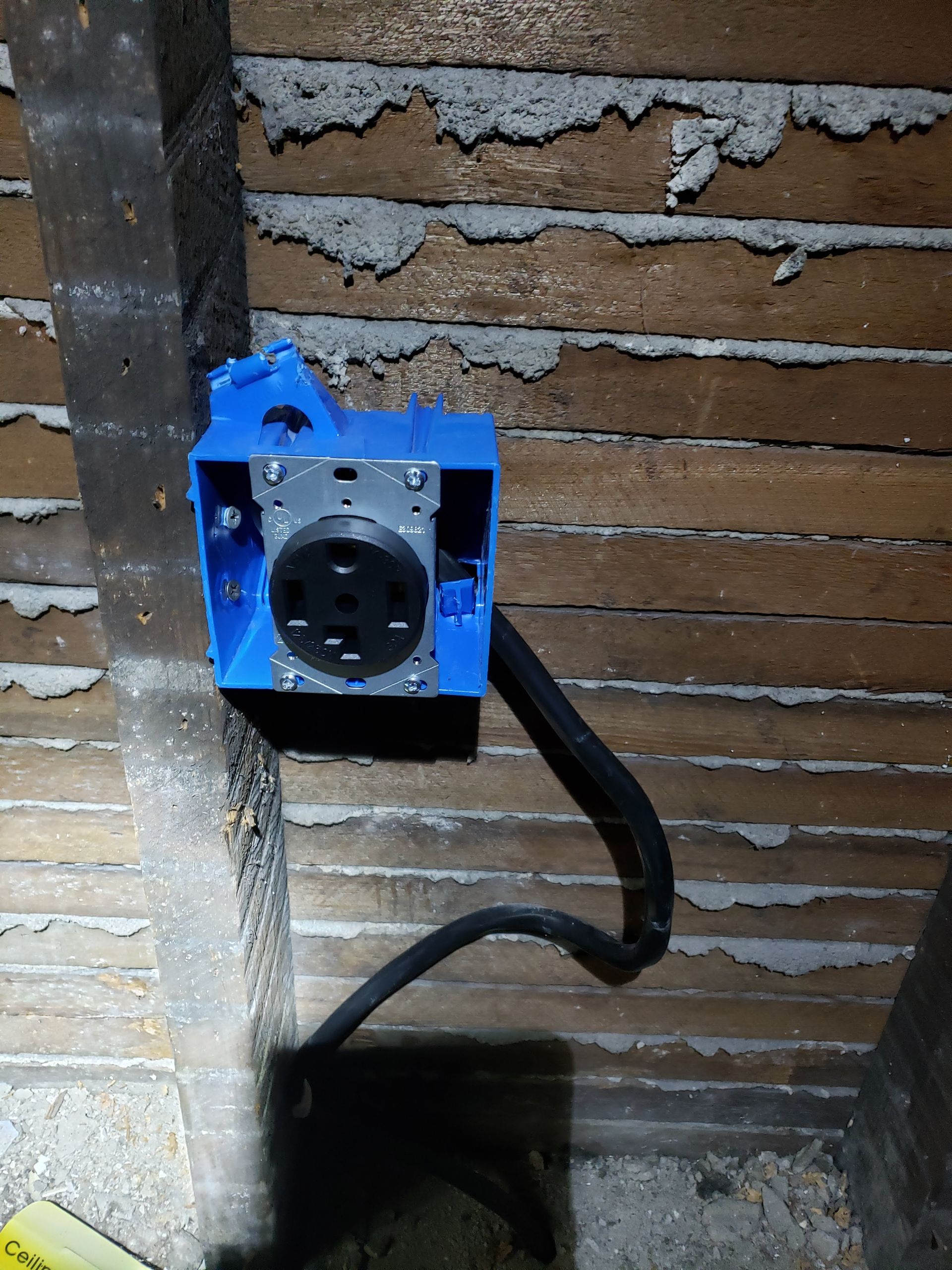 A blue box with a black cord attached to it is on a wooden wall.