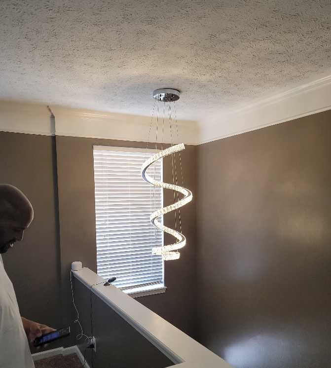 A man is standing in a room with a spiral light hanging from the ceiling.