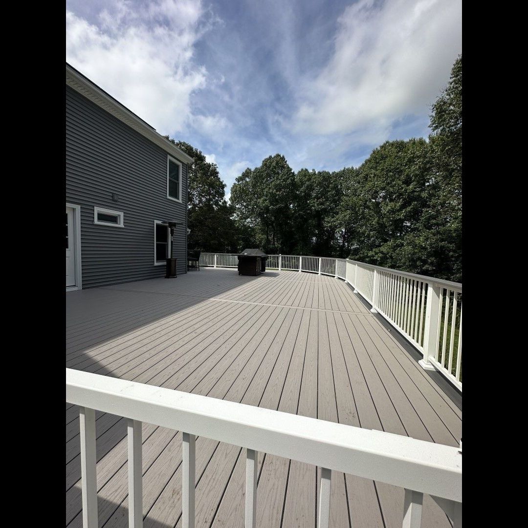 A large deck with a white railing and a house in the background.