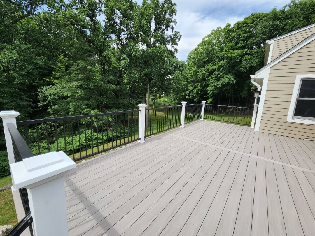 There is a large deck with a railing and trees in the background.