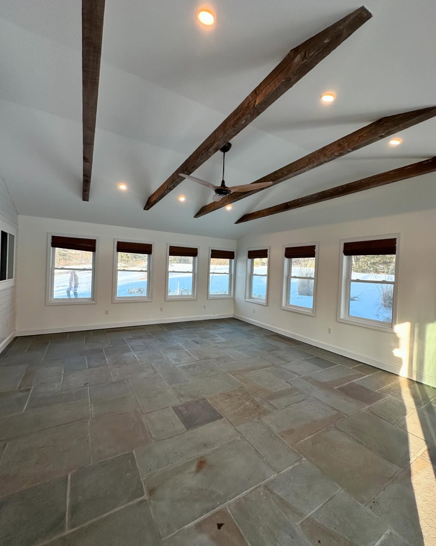 A large empty room with a ceiling fan and lots of windows.