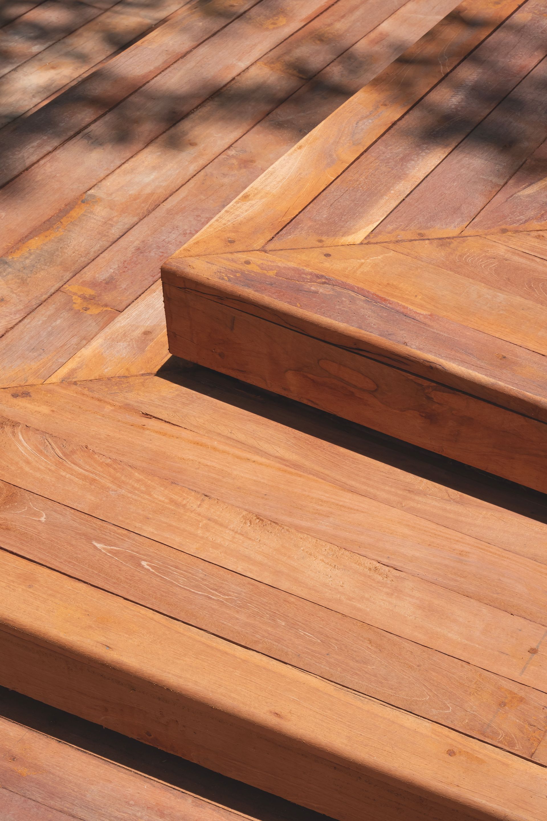 Wooden deck with steps and sunlight dappling the surface.
