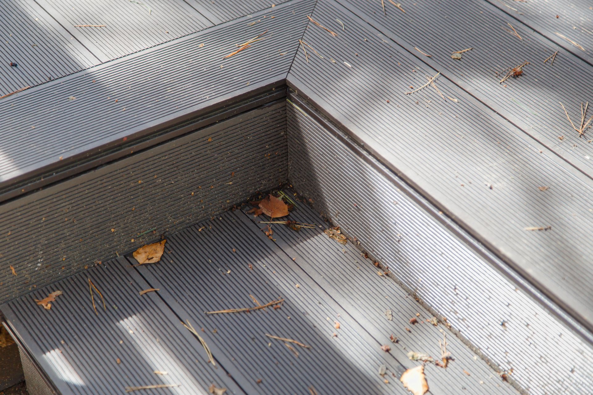 Gray textured deck boards with a corner, scattered with leaves.