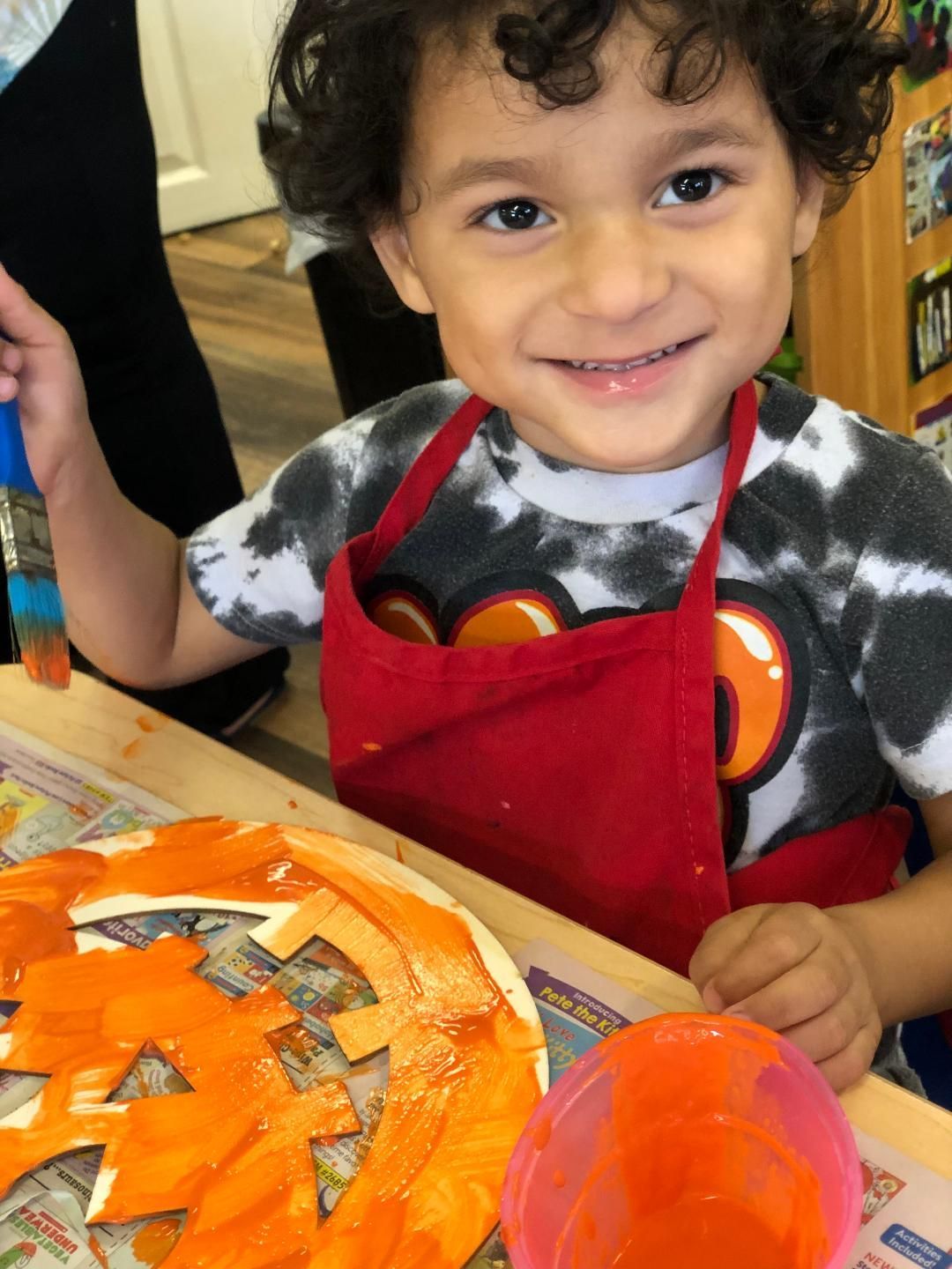 Young child with curly hair, painting orange pumpkin, smiling in a craft activity.