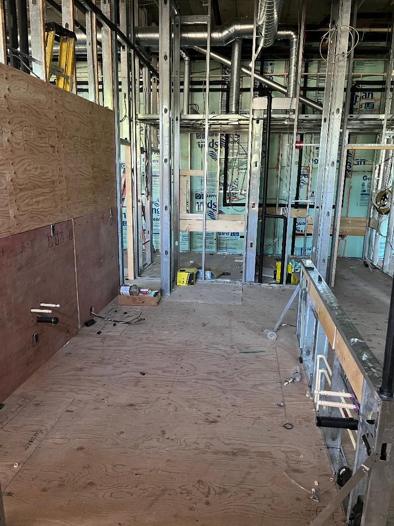 Construction site with exposed metal framing, ductwork, and plywood walls.