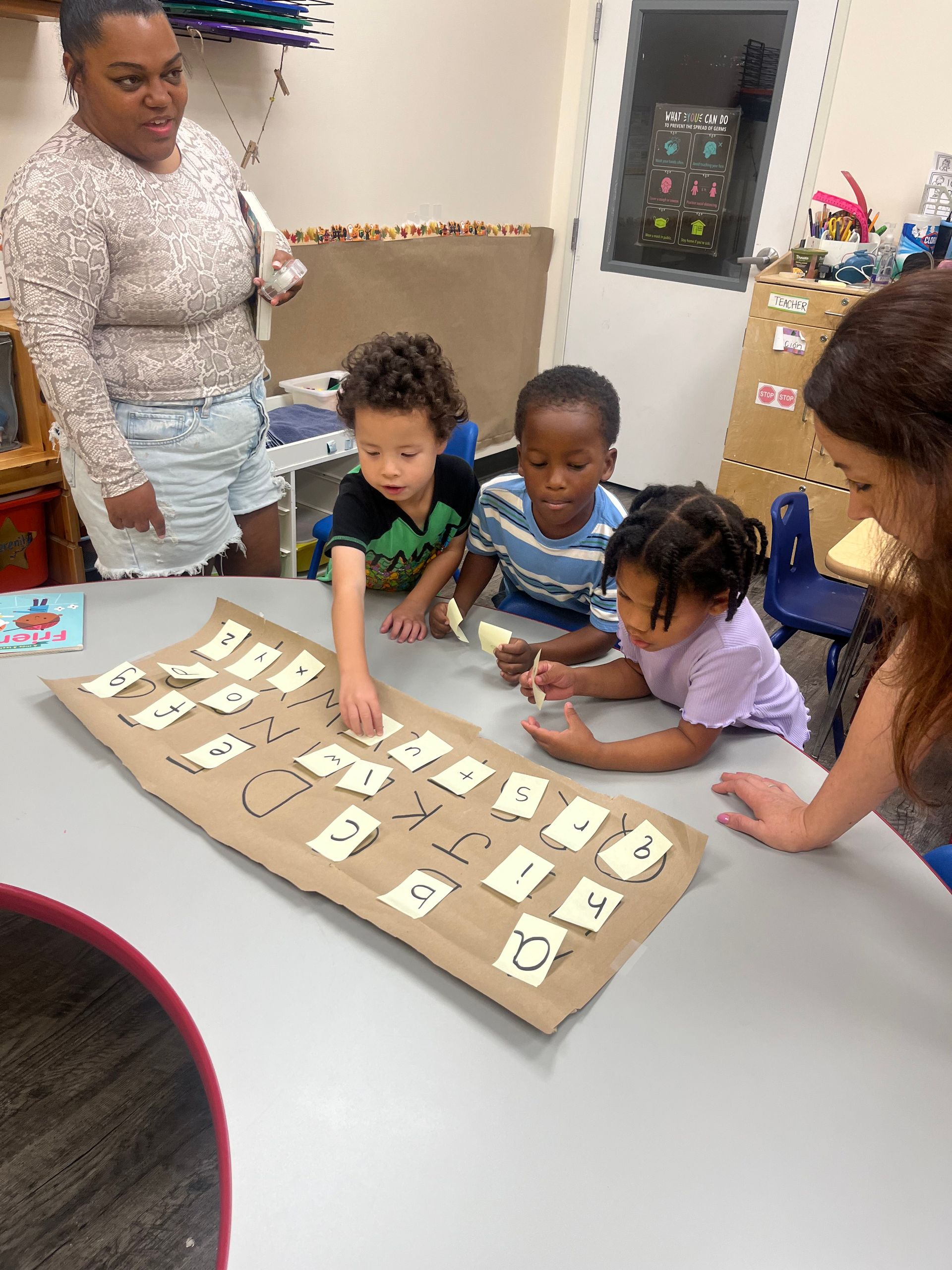 Children and adults at a table working with numbers. Kids point at cards on a brown surface.
