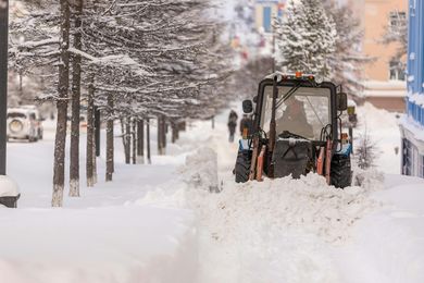 A snow plow is clearing snow from a sidewalk.