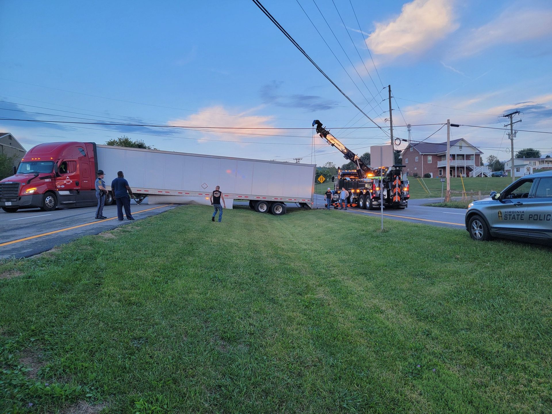 Semi-truck trailer stuck under power lines; tow truck assisting.